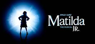 A graphic with a black background. At left we see a young girl standing proudly and silhouetted by a blazing blue-white light. At right in white lettering are the words "Road Dahl's Matilda Jr., The Musical."